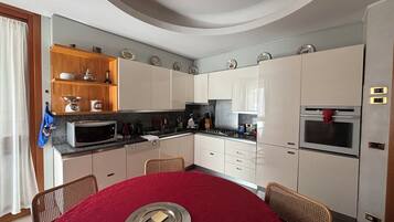 Cocina compacta con armarios blancos, microondas, estufa y una mesa de comedor roja para dos.