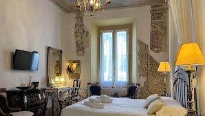 A well-appointed hotel room with a large bed, a desk with a chair, a television, and a chandelier. - Verona Journeys (Verona)