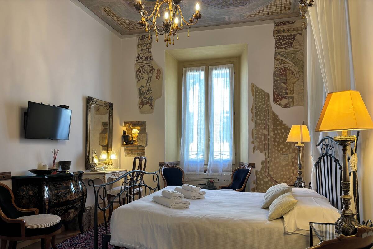 A well-appointed hotel room with a large bed, a desk with a chair, a television, and a chandelier.