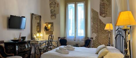 A well-appointed hotel room with a large bed, a desk with a chair, a television, and a chandelier.