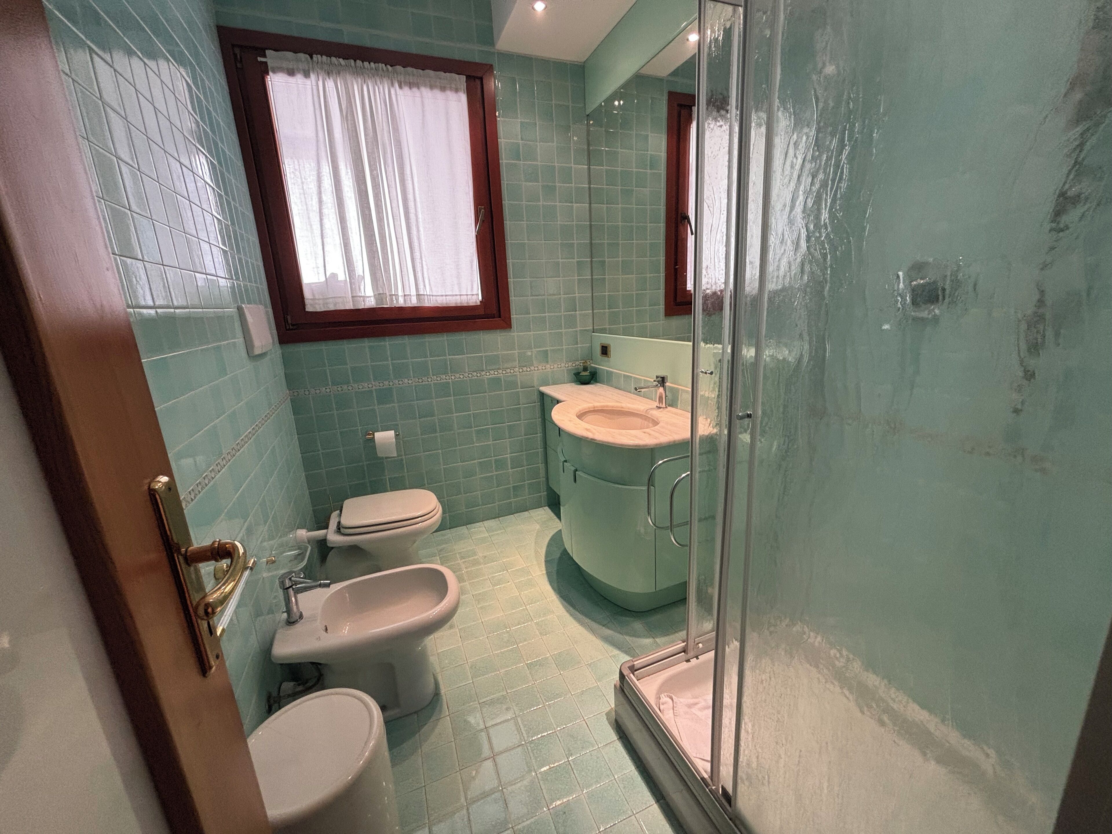 Un baño con inodoro, bidé y zona de ducha con mampara de vidrio.