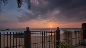 Blick auf einen Strand mit einem Zaun, Palmen und einem Sonnenuntergang.