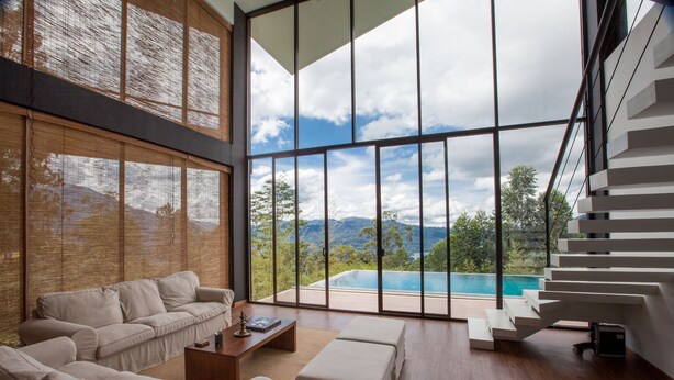 Ein großzügiger Wohnraum mit einem großen Fenster und Blick auf Pool und Berge.