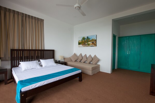 A bedroom with a large bed, a nightstand, a sofa, a painting, and a teal wardrobe. - Ramboda Villa (Kothmale)