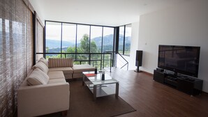 Ein modernes Wohnzimmer mit Sofa, Couchtisch und Fernseher, mit großen Fenstern und Blick auf die Berge.