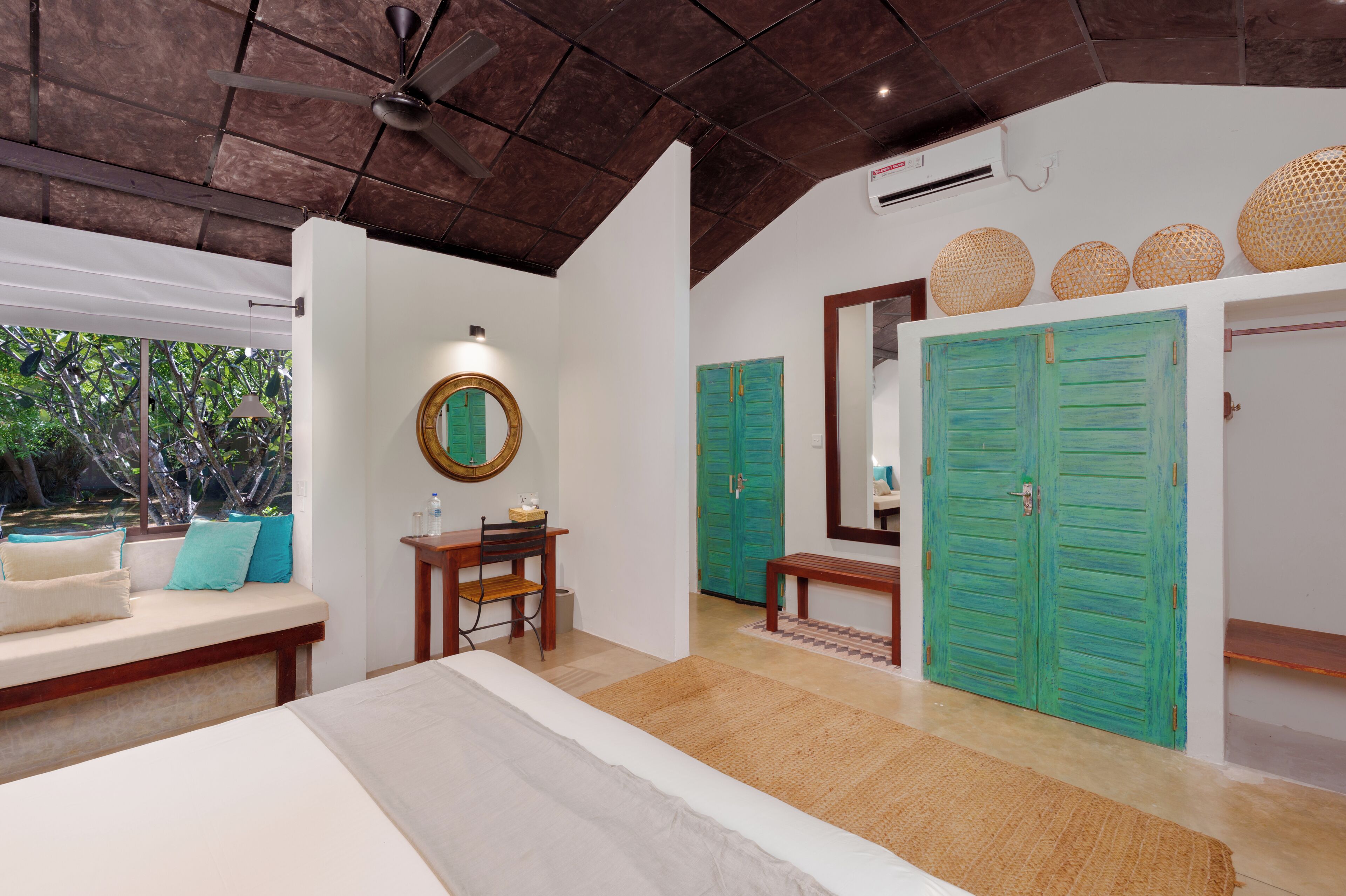 A bedroom with a bed, a desk, a chair, a bench, a mirror, and two green doors.