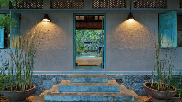 Un edificio con base de piedra, puerta de madera y vista a un jardín a través de una ventana.