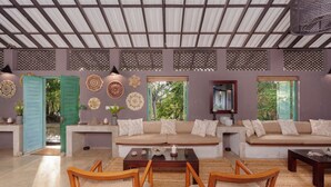 Amplia sala de estar con un conjunto de sofás, sillas de madera, una mesa de centro, decoración en la pared y vistas a través de puertas abiertas.