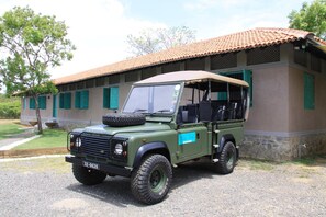 A green Land Rover Defender parked in front of a building with a tiled roof and green shutters. - Yala Villa (Kirinda)