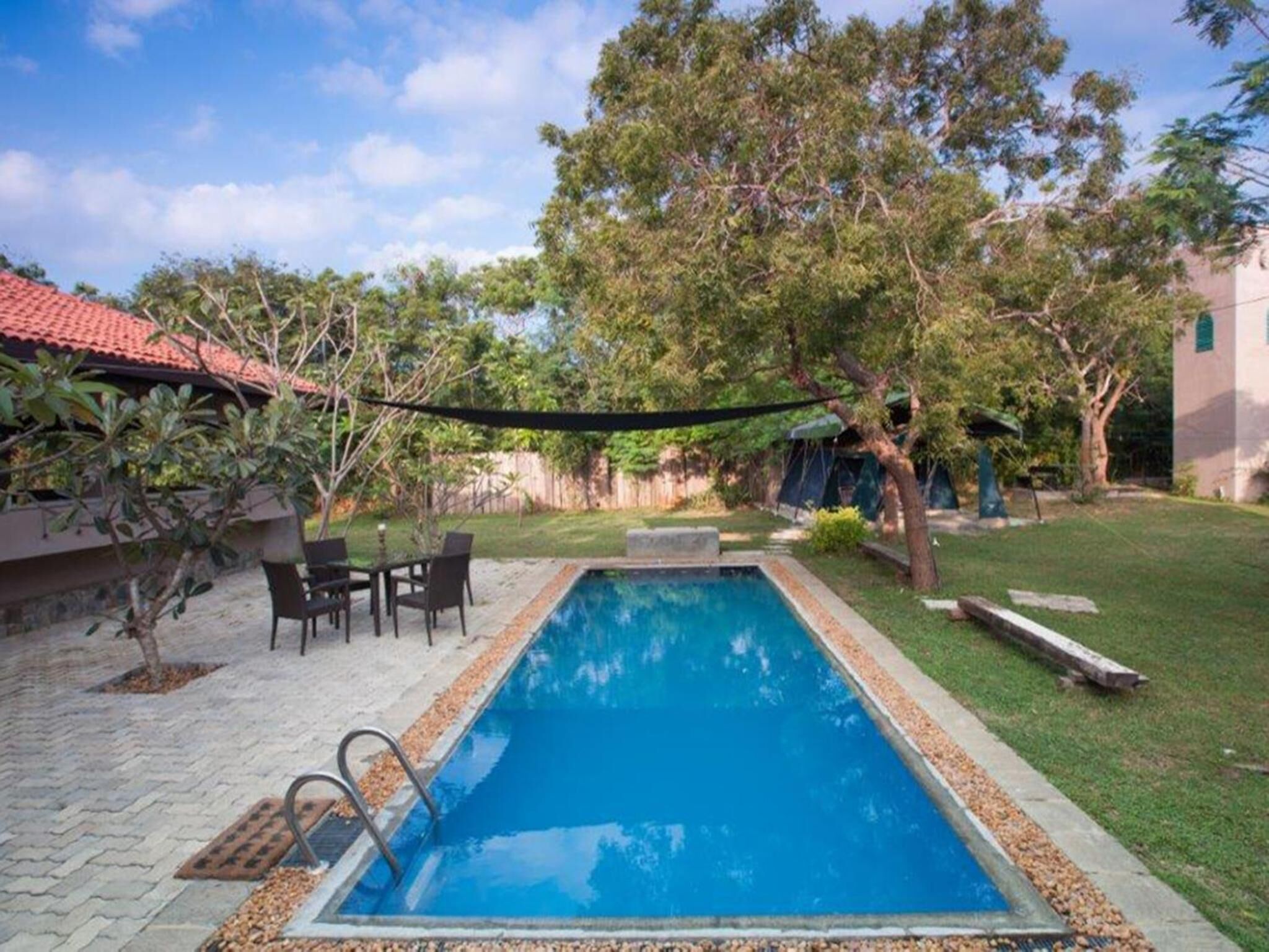 A rectangular swimming pool with a tiled deck, surrounded by a grassy area and trees.