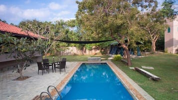 A rectangular swimming pool with a tiled deck, surrounded by a grassy area and trees.