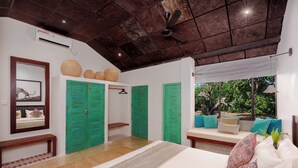 Un dormitorio con cama, puertas verdes, ventilador de techo y ventana con vistas a árboles.