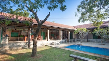 Una casa con piscina, terraza techada y un árbol en el jardín.