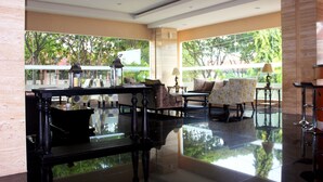 A spacious lobby with a polished floor, comfortable seating, and large windows offering a view of greenery outside. - Demelia Hotel (Makassar)
