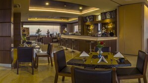 A modern restaurant with a bar area, wooden chairs, and a view of the cityscape. - Demelia Hotel (Makassar)