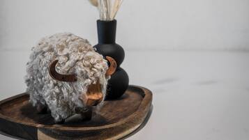 A rustic decor setup with a woolly sheep sculpture, a black vase with dried plants, and a wooden tray.