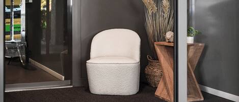 Un interior moderno con una silla blanca con textura, una cesta tejida y una mesita de madera con plantas secas.