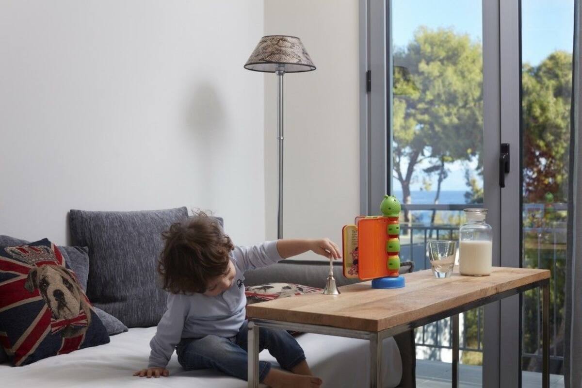 A child playing with toys on a wooden table in a room with a view of trees and a balcony.