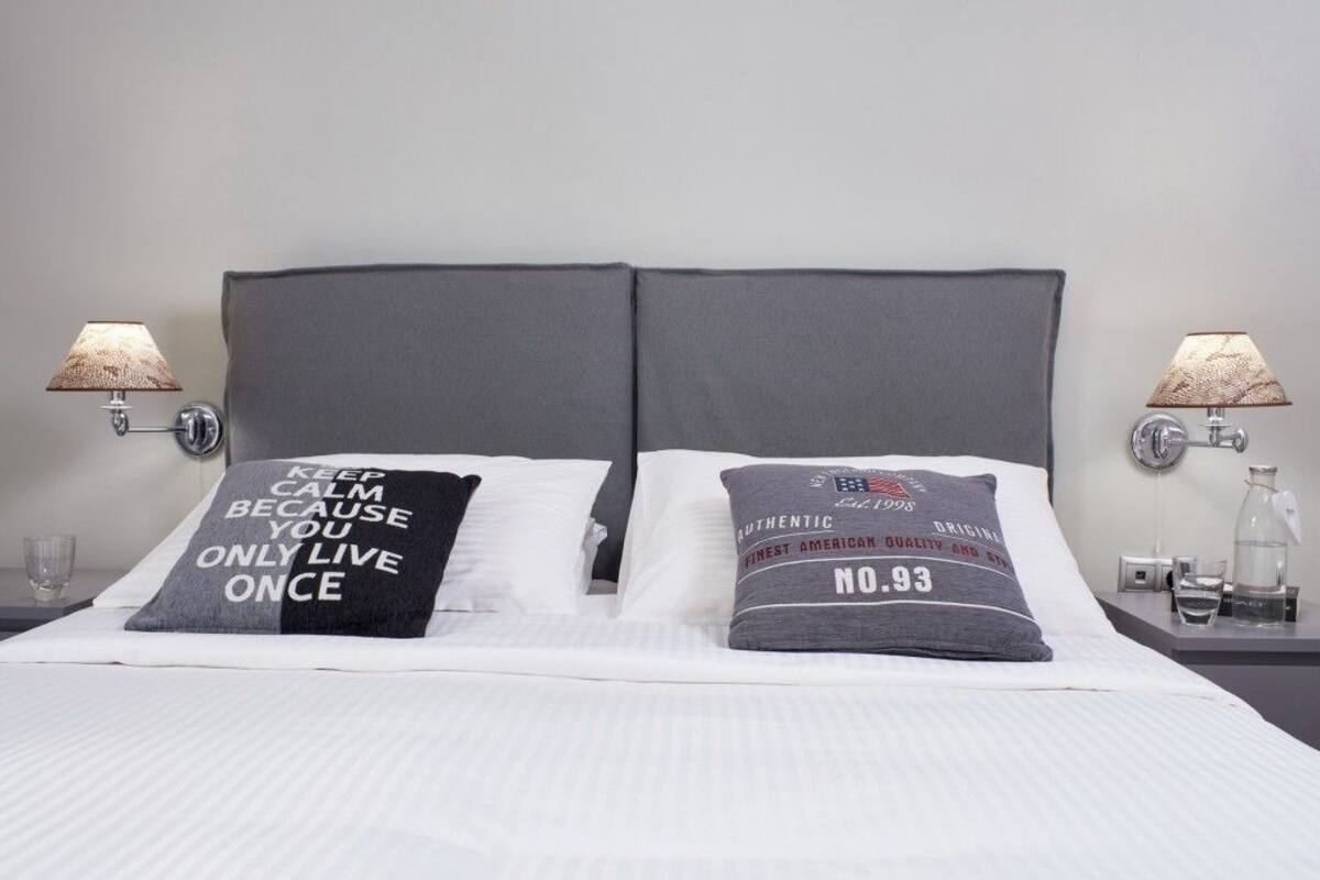 A neatly made bed with two pillows, each with a motivational quote, and two wall-mounted lamps on either side.