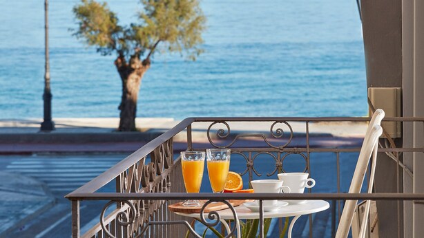 Varanda com mesa posta para o café da manhã, com vista para um corpo d'água e uma árvore.