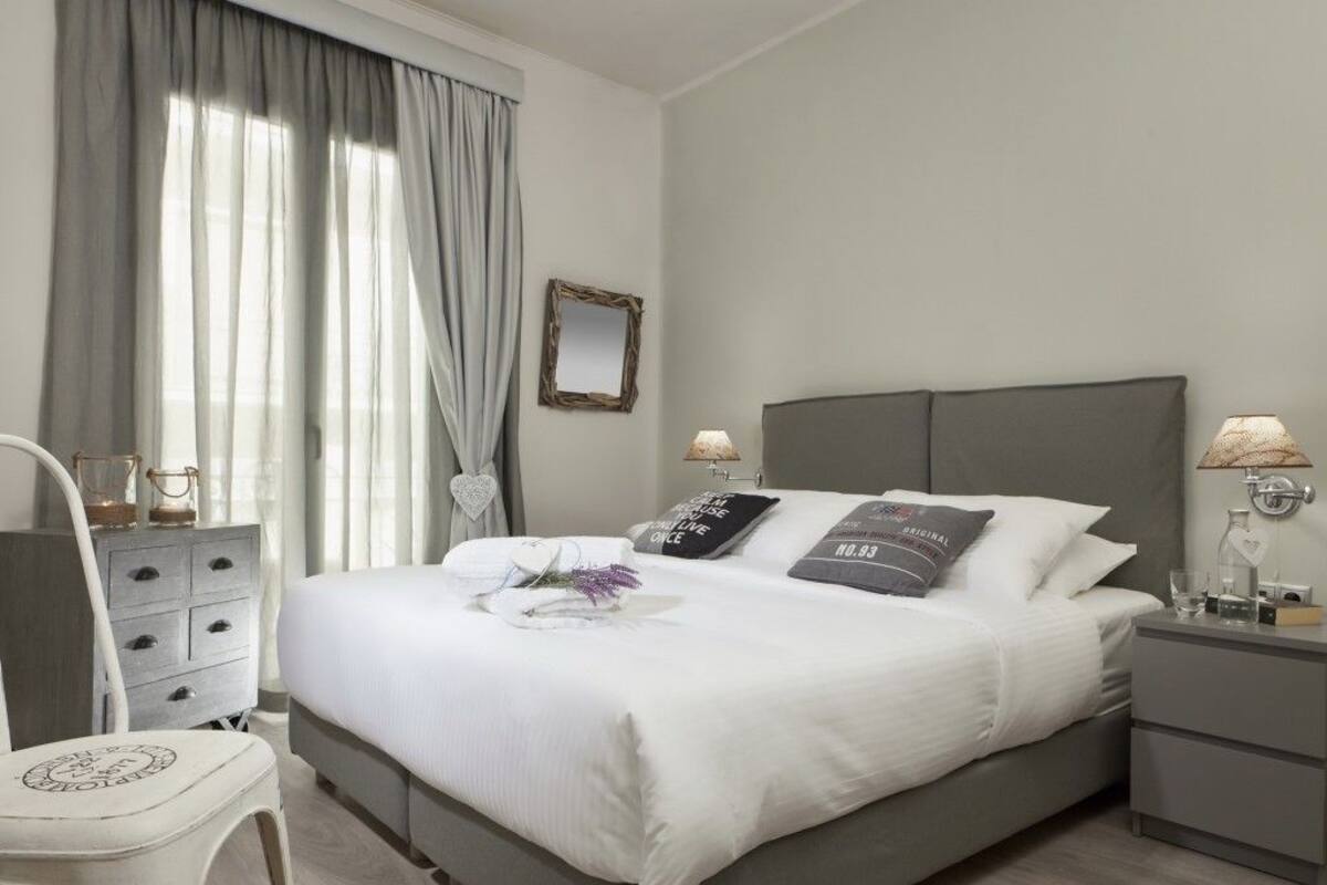 A neatly arranged bedroom with a bed, bedside tables, a chair, and a window with curtains.