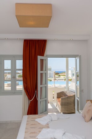 Un dormitorio con cama, ventana con cortinas y vistas a una piscina y edificios.