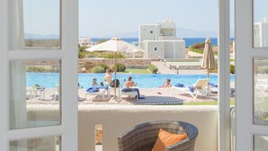 A balcony with a wicker chair and a small table, overlooking a swimming pool area with lounge chairs and umbrellas. - Sun and Moon Villas (Naxos)