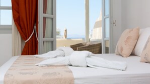 A hotel room with a bed, a view of the sea, and a wicker chair. - Sun and Moon Villas (Naxos)