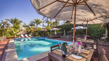 A poolside dining area with a table set for two, surrounded by lounge chairs and umbrellas.