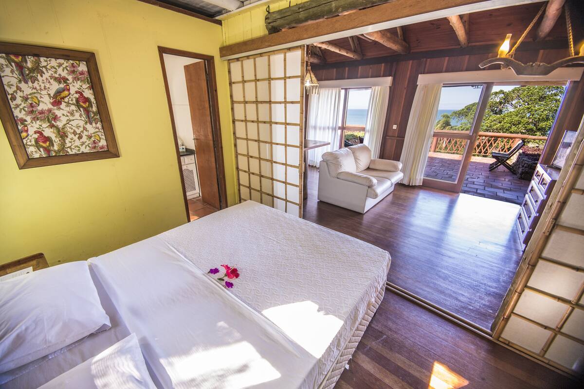 Ein Zimmer mit einem Bett, einem verschiebbaren Shoji-Bildschirm, einem Balkon mit einem weißen Stuhl und Blick aufs Meer.