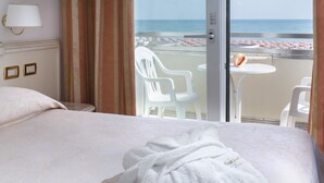 Ein Hotelzimmer mit Bett, Bademantel, Blick auf den Strand und einem Balkon mit Stühlen und Tisch.