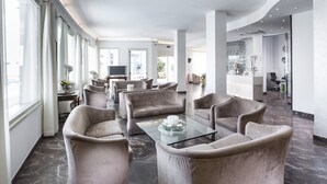 Eine großzügige Lobby mit modernem Design, inklusive einer Sitzecke mit bequemen Ohrensesseln und einem Glastisch.