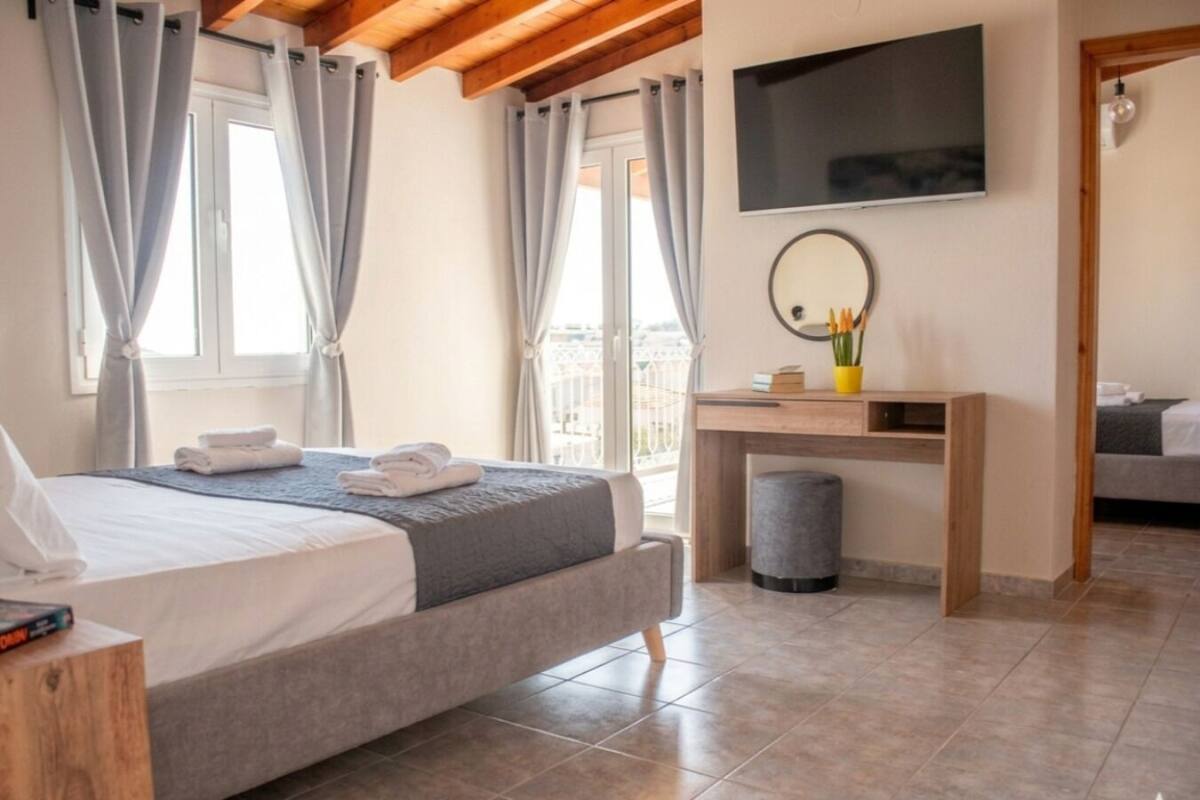 A bedroom with a bed, a desk, a mirror, and a TV.