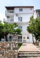 Un edificio de varios pisos con balcones, un muro de piedra y una entrada pavimentada.