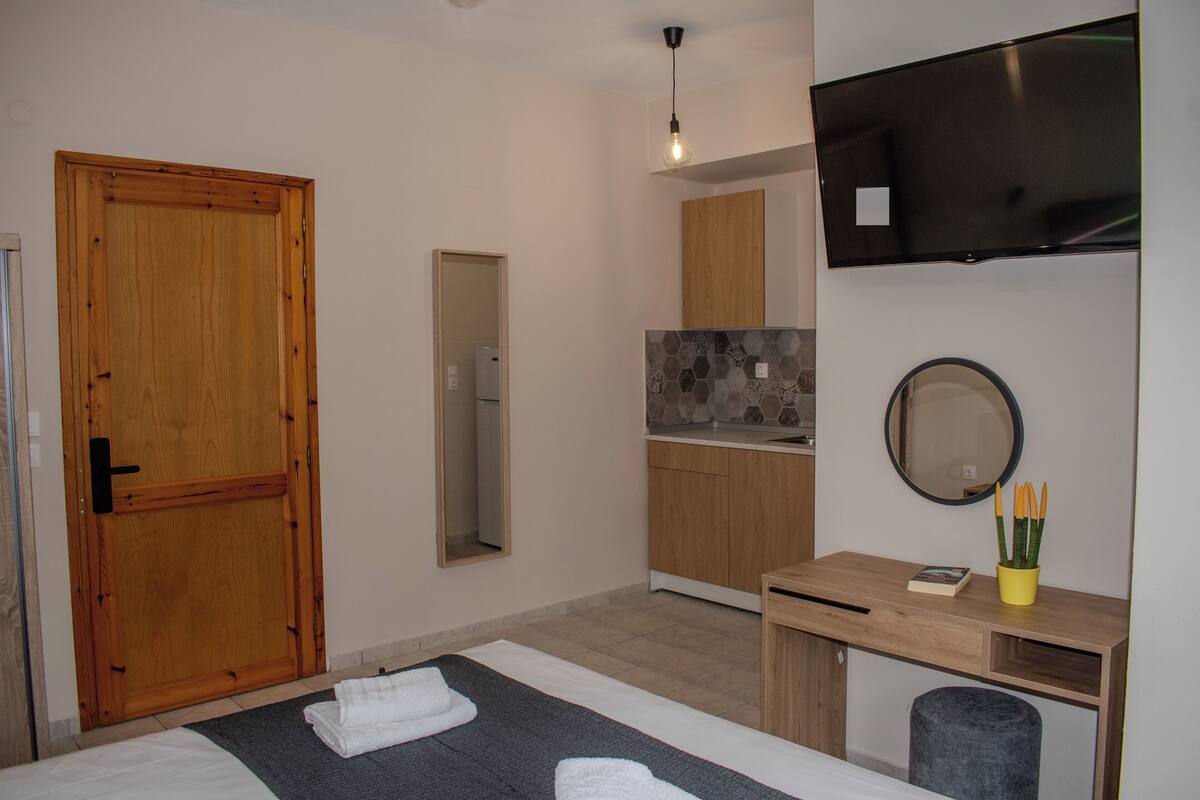 A modern room with a bed, a desk, a mirror, a TV, and a wooden door.