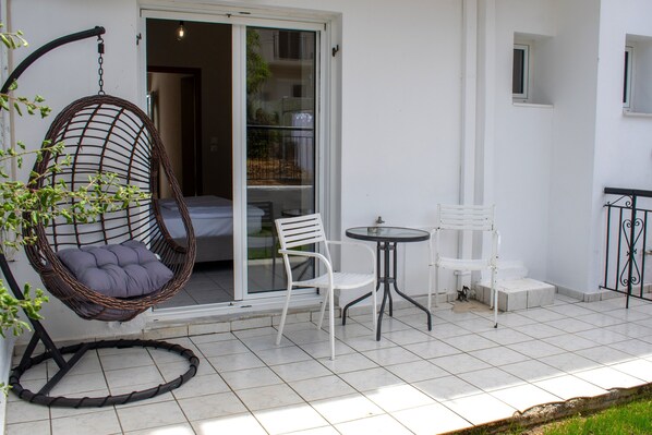 A patio with a hanging chair, two white chairs, a small table, and a glass door leading to an interior space. - Eos Skiathos (Skiathos)