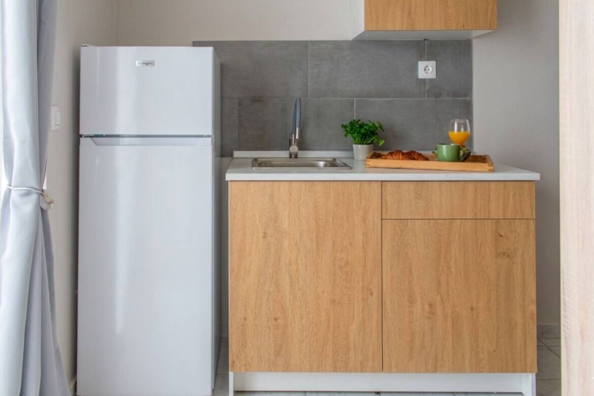 A kitchen with a white refrigerator, a sink, wooden cabinets, a potted plant, and a tray with food and a glass of orange juice.