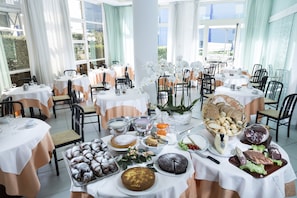 A dining area with multiple tables set for a meal, featuring a variety of food and drinks. - Hotel Mocambo (Cervia)