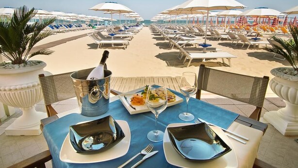 A table set for two with a view of the beach and umbrellas. - Hotel Mocambo (Cervia)