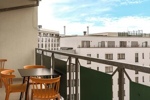 A balcony with a table and chairs, overlooking a cityscape with buildings.