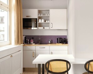 A compact kitchen with white cabinets, a built-in microwave, a coffee maker, and a window with curtains.