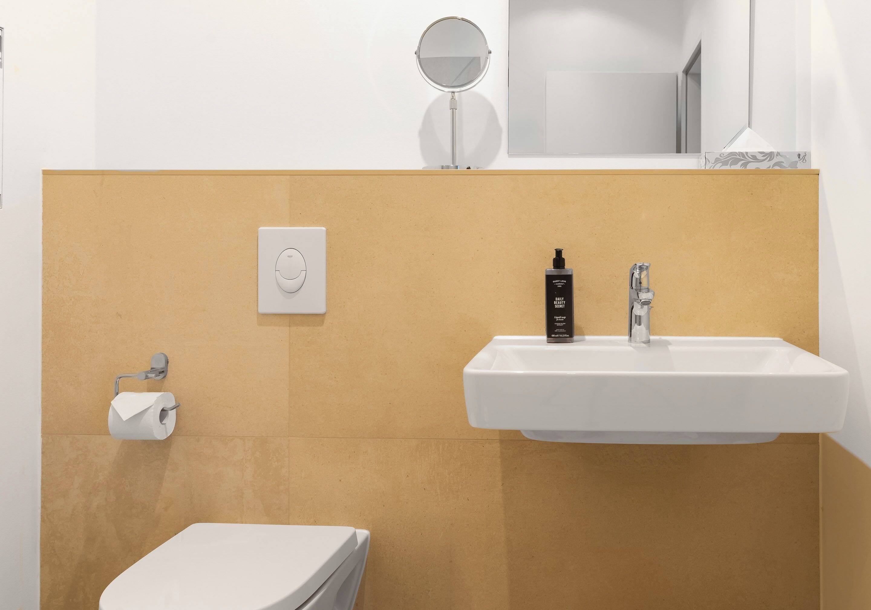 Et badeværelse med en hvid vask, et spejl, et toilet og en papirhåndklædedispenser.