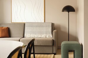 A modern living room with a sofa, a small table, a floor lamp, and a green ottoman.