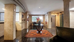 Un vestíbulo con columnas de mármol, un mostrador de recepción, una mesa de centro y una alfombra estampada.