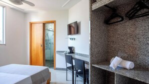 Habitación de hotel con cama, escritorio con silla, televisor y zona de ducha.