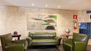 Un vestíbulo con un sofá de cuero verde, dos sillones, una mesita, un extintor y un cuadro abstracto grande en la pared.