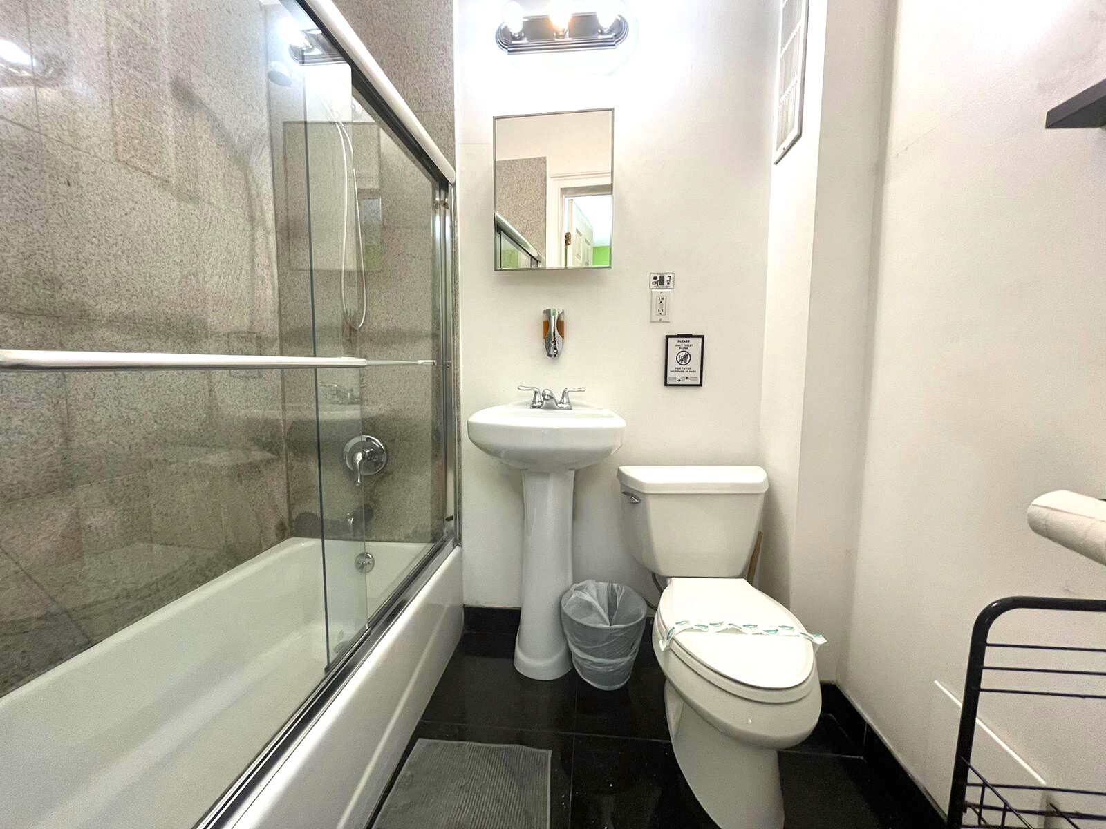 Ein Badezimmer mit einer Duschkabine, einem Standwaschbecken, einer Toilette und einem Mülleimer.