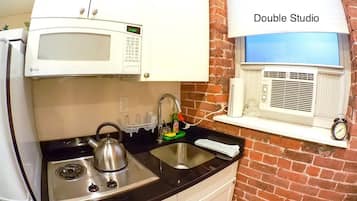 A kitchen with a stove, kettle, sink, microwave, and a window with a view.