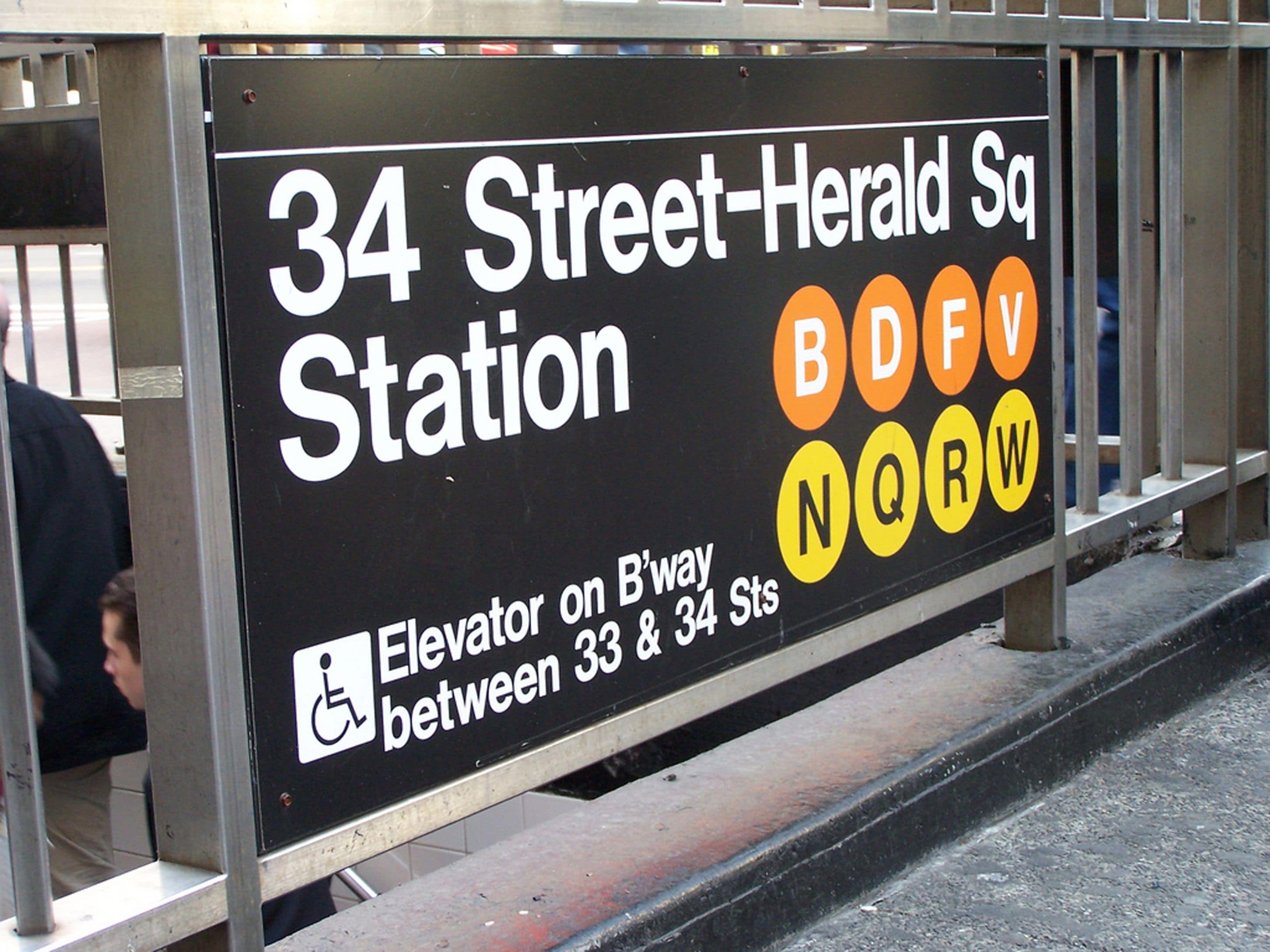A sign for 34 Street-Herald Sq Station with an elevator on B-way between 33 & 34 Sts.