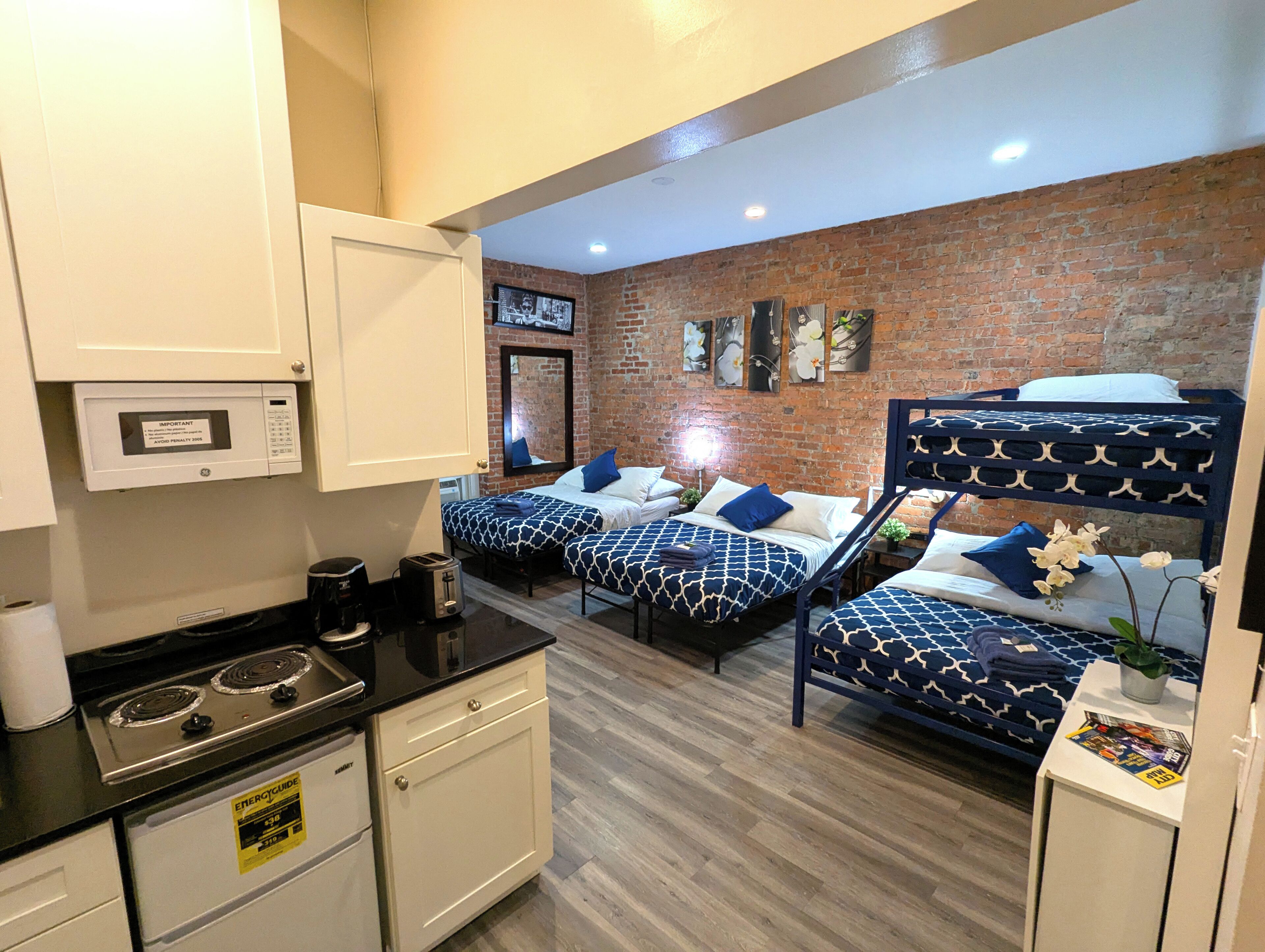 Een kleine hotelkamer met twee bedden, een kitchenette, een bakstenen muur en een kleine badkamer.